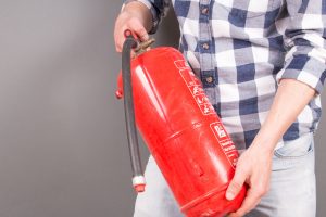 Der Brandschutzratgeber erklärt richtiges Verhalten im Brandfall. © Waler; Quelle: Fotolia.com Ein Mann zeigt einen Feuerlöscher, für das richtige Verhalten im Brandfall